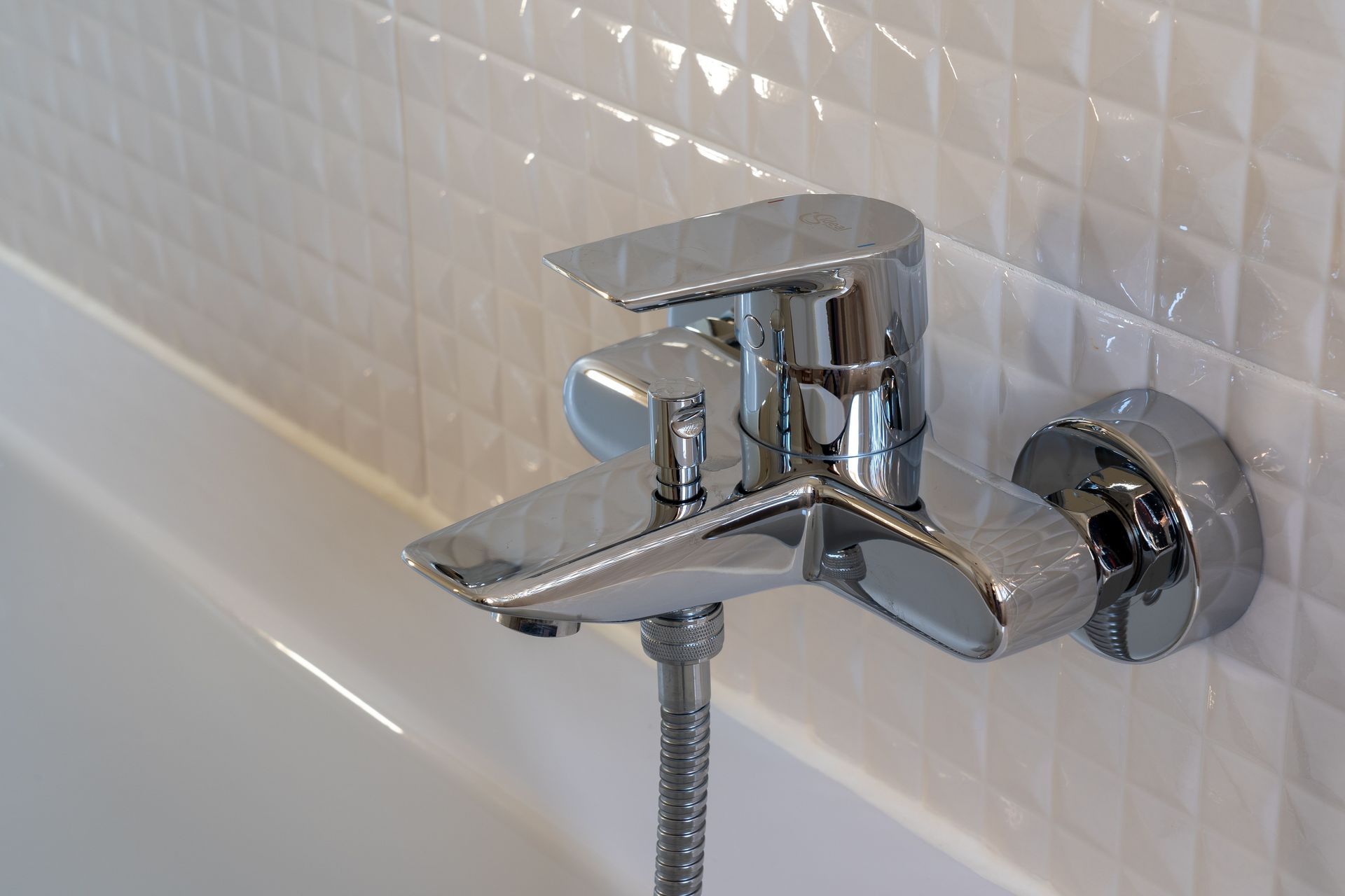 Close-up of a contemporary chrome faucet in a modern bathroom with white geometric tiles.